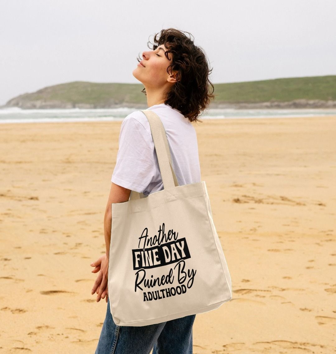 White tote bag with text "Another Fine Day Ruined By Adulthood" (person)